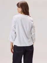 Remera de algodón color blanco, con cuello redondo y mangas tres cuartos con volados escalonados y detalles de pespuntes.