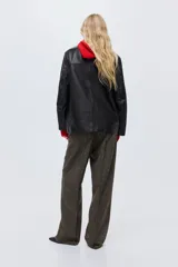 Pantalón de tiro alto en color marrón oscuro, con diseño de pierna recta y pliegues frontales cosidos. Presenta bolsillos de parche delanteros con botones decorativos dorados.