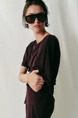 Top de crepe fluido en color bordó, con cuello barco, manga corta y diseño asimétrico con drapeado lateral.