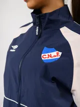 Campera deportiva Umbro del Club Nacional de Football, con diseño de bloques de color en azul marino y blanco. Presenta cuello alto, cierre frontal completo, bolsillos laterales y el escudo del club junto al logo de la marca en el pecho.