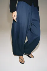 Pantalón de tiro medio con pierna ancha, confeccionado en mezcla de lyocell y viscosa. Cuenta con cintura elástica ajustable con cordones y bolsillos laterales ocultos en la costura.