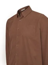 Camisa de manga larga confeccionada en tejido de cotele de algodón orgánico, color marrón castaño. Presenta cuello camisero con botones, cierre frontal con botones, puños abotonados y un bolsillo frontal en el pecho con detalle bordado.