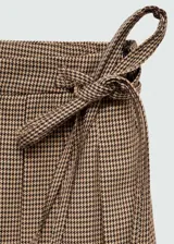 Falda corta de tiro medio con diseño de tablas y estampado de pata de gallo en tonos marrones. Presenta un cierre lateral de cremallera y un detalle de lazo ajustable en la cintura.
