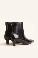 Bota de caña corta confeccionada en cuero vacuno color chocolate con acabado brillante. Presenta punta fina, cierre posterior y taco chupete bajo.
