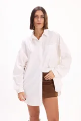 Camisa de corte oversize, color blanco, con cuello clásico, cierre frontal de botones y mangas largas con puños abotonados.