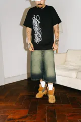 Bermuda de jean estilo baggy con lavado verde desgastado. Presenta grandes bolsillos traseros con bordados en hilo rojo que simulan caracteres chinos.