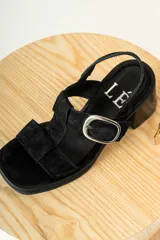 Sandalias de gamuza negra con taco cuadrado y plataforma. Presentan un diseño de tiras anchas con una hebilla metálica plateada ajustable en el lateral.