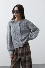 Cardigan de tejido de punto color marrón chocolate, con diseño de trenzas en el frente y mangas. Presenta cuello redondo, cierre frontal con botones al tono y puños acanalados.