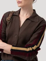 Sweater de punto color marrón con cuello camisero y cierre frontal de botones. Presenta detalles de tejido calado en las mangas con franjas laterales en contraste y terminaciones en crochet en el cuello y la tapeta.