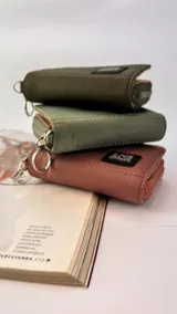 Billetera corta de diseño capitoneado con cierre perimetral y solapa frontal. Cuenta con compartimentos internos para tarjetas y billetes, e incluye una correa de mano desmontable.