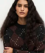 Suéter de punto pesado con diseño de cuadros argyle en tonos marrón y negro, con detalles de puntos claros. Presenta un corte oversize, cuello redondo acanalado y mangas largas.
