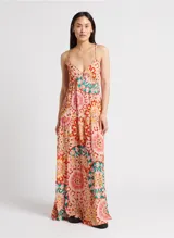 Vestido largo con estampado caleidoscópico en tonos rosa, rojo y verde. Presenta tirantes finos, escote en V, corte imperio y falda con volantes. Incluye detalle de trenzas en el pecho y la cintura que se anudan en la espalda descubierta.