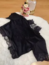 Top de terciopelo negro con cuello alto, detalles de encaje en el cuello y mangas, y paneles de microtul. Presenta espalda descubierta.