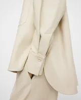 Sobrecamisa de efecto piel color beige, de corte recto y holgado, con cuello mao, manga larga, cierre frontal de botones y un bolsillo aplicado en el pecho.