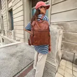 Mochila de cuero sintético color marrón, con compartimento principal con cierre, bolsillo frontal con cierre horizontal y bolsillo lateral vertical con cierre.