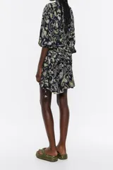 Vestido corto negro con estampado paisley en tonos amarillo y lila, escote en pico pronunciado con fruncido, manga larga con botón en puño, cierre con cremallera invisible, cintura con maxifruncido y falda con vuelo.