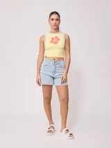 Musculosa crop amarilla con estampado de flor roja en el frente y ribetes grises en cuello y sisas, de la marca Rusty.