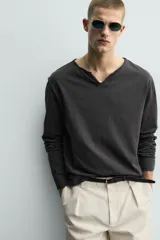 Camiseta de manga larga con corte relajado, confeccionada en algodón. Presenta un cuello redondo amplio con acabado irregular y detalle de botones frontales a tono.