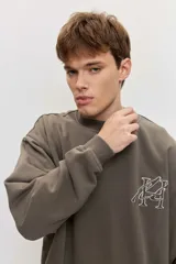 Buzo de friza color gris oscuro, de corte oversize, con cuello redondo y diseño liso. Cuenta con un pequeño bordado en el pecho.