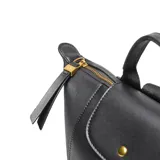 Mochila negra de material símil cuero (PU) con herrajes dorados. Presenta un asa corta superior, correas traseras regulables y un bolsillo frontal con solapa que se cierra con un broche metálico. En el centro de la solapa lleva un logo metálico con las letras "XL".