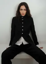 Chaqueta entallada de color negro con cuello mao y cierre frontal de botones metálicos efecto joya. Presenta diseño de largo medio, manga larga y forro interior.