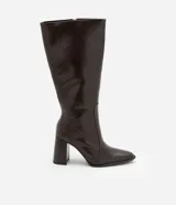 Bota de caña alta color marrón chocolate, confeccionada en material sintético con acabado brillante. Tiene punta almendrada, cierre lateral con cremallera y tacón bloque alto.