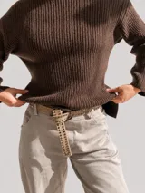 Pantalón de corte recto y holgado en color beige, con cintura elástica y dobladillo en los tobillos. Incluye un cinturón de cuero sintético con tachas metálicas decorativas.