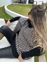 Poncho oversize con cuello alto negro, diseño geométrico en blanco y negro, bolsillo lateral y detalle de bloques de color en gris y negro.