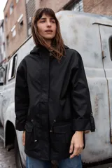 Parka liviana color beige con capucha, cierre frontal con botones, bolsillos delanteros con tapa y ajuste en la cintura. Presenta mangas con puños vueltos y detalle de botones.
