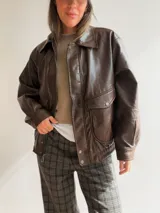 Campera de efecto cuero en color marrón chocolate, con diseño de corte relajado, cierre frontal, bolsillos amplios con solapa y terminaciones elastizadas en puños y ruedo.