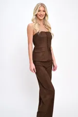 Conjunto de dos piezas confeccionado en tela agamuzada. Incluye un top strapless con cierre frontal de botones y bolsillos decorativos, y un pantalón de corte recto y tiro alto.