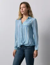 Camisa de gasa celeste con estampado de rayas verticales en tonos azules, rosas y verdes. Tiene cuello con solapa, escote en V, abertura central con botones, bolsillo aplicado en el pecho y terminación anudada en la parte delantera.