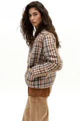 Chaqueta reversible con un lado de twill de lana a cuadros en tonos beige, marrón y gris, con vivos en pana color camel y bolsillos frontales. El otro lado es de algodón capitoneado con estampado de arabescos. Tiene cuello a la base y botones metálicos a presión escondidos.