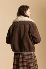 Campera de gamuza color marrón con cuello de corderito sintético en color crema. Presenta cierre frontal, bolsillos laterales con broches metálicos y puños rectos.