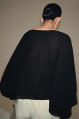 Cuerpo de punto negro con cuello barco, sisa ancha y mangas largas amplias con puños ajustados.