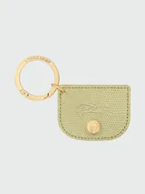 Llavero Longchamp de la línea Épure, con argolla metálica dorada grabada y dije de cuero texturizado en color verde claro con el logo de la marca grabado y un botón decorativo central.