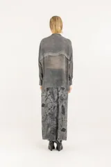 Camisa boxy oversize de viscosa y seda en color gris, con detalles de satén de viscosa y doble canesú en el frente y la espalda, teñida en frío. Tiene cuello mao, cierre frontal con botones, hombros caídos y mangas largas con puño, confeccionada en tejido liviano semitransparente.