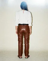 Pantalón de cuero vacuno color marrón, de corte recto y tiro medio. Presenta una cintura con detalle de presillas fruncidas en contraste negro y forrería interna de satén.