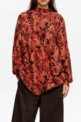 Jersey de pelo con cuello alto, manga larga y diseño holgado. Presenta un estampado animal print difuminado en tonos rojizos y negros.