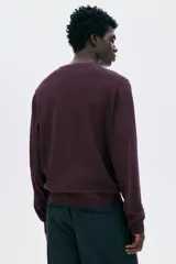 Buzo de punto fino color borgoña, con cuello redondo y corte regular.