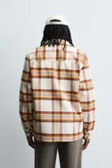 Camisa de corte relajado confeccionada en tejido con acabado de franela. Presenta diseño de cuadros en tonos beige, marrón y amarillo, cuello solapa, manga larga con puños abotonados, bolsillos plastrón en el pecho y cierre frontal de botones.