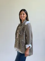 Sweater de punto color visón con diseño superpuesto, que incluye una bufanda integrada y detalles de encaje floral en el frente. Presenta mangas tres cuartos con puños abotonados y un corte holgado.