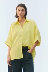Camisa oversize blanca de lino, con corte cuadrado, mangas raglán cortas con puños anchos, aberturas laterales y cierre frontal de botones.