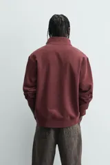 Sudadera roja de corte regular, con cuello alto y cierre frontal de cremallera. Manga larga y terminaciones en rib.