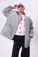 Campera acolchada color gris claro, con cuello mao y cierre frontal con botones a presión. Tiene bolsillos laterales y corte holgado.