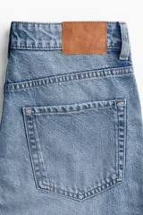 Jean de corte wide leg con diseño de cinco bolsillos, confeccionado en denim de algodón rígido. Presenta un lavado claro con efecto desgastado y un detalle de rotura en la rodilla izquierda. Cuenta con cintura clásica, cierre de botón y bragueta.