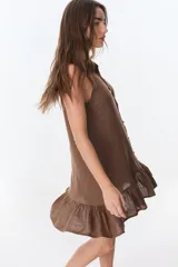 Vestido corto sin mangas de lino, con cuello camisero, cierre frontal con botones y detalle de volado en el ruedo.