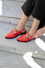 Zapatos tipo mules color rojo con punta cuadrada, dos tiras con hebillas plateadas y detalle de ojalillos metálicos.