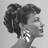 Par de aros colgantes con forma abstracta irregular, hechos de acrílico blanco con diseño interior de manchas negras y plateadas con glitter.