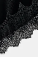 Vestido midi de terciopelo negro con escote en pico y tirantes finos ajustables. Presenta un diseño asimétrico en el bajo con aplicación de encaje a tono y espalda con tiras cruzadas.